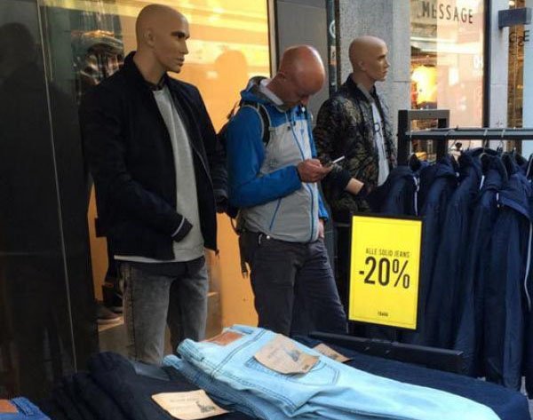 Bald man texting around a few mannequins and he looks like he is one of them.