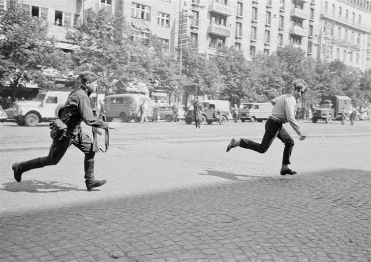 In 1968, a Soviet soldier chases a young man through the streets of Prague, for throwing stones at a tank.