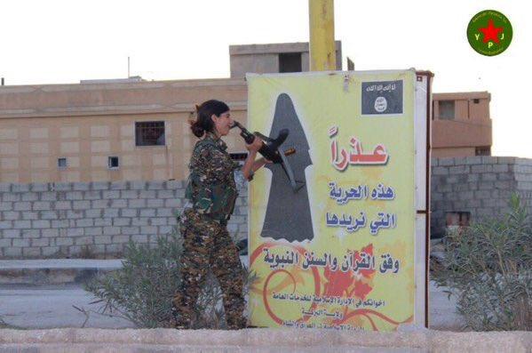 A female Kurdish fighter destroys an ISIS sign with instructions on how women should dress, northeast Syria, November 2015