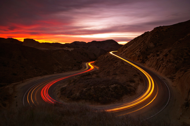 Car lights illuminate a sharp bend along the mountainside.