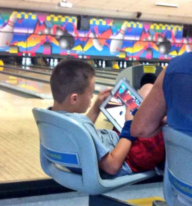 This kid playing on a bowling app in a real bowling alley