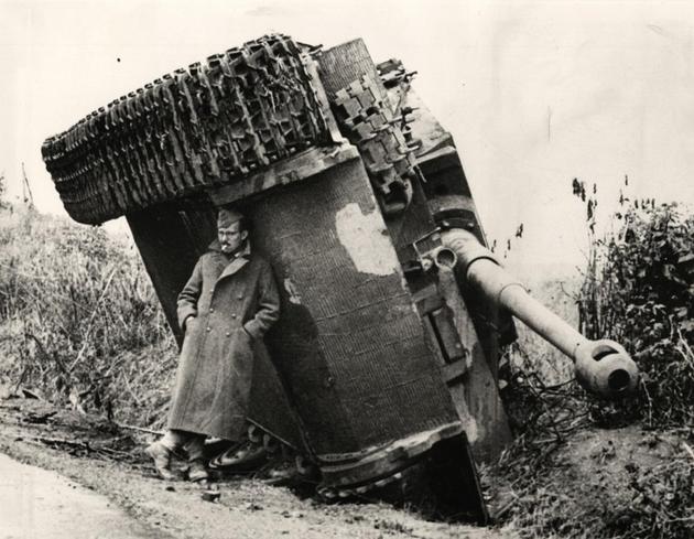 A British soldier hiding from the rain under an overturned Tiger tank. Italy, 1944.