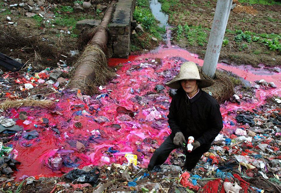 A Woman Collects Plastic Bottles Near A River Polluted With Reddish Dye