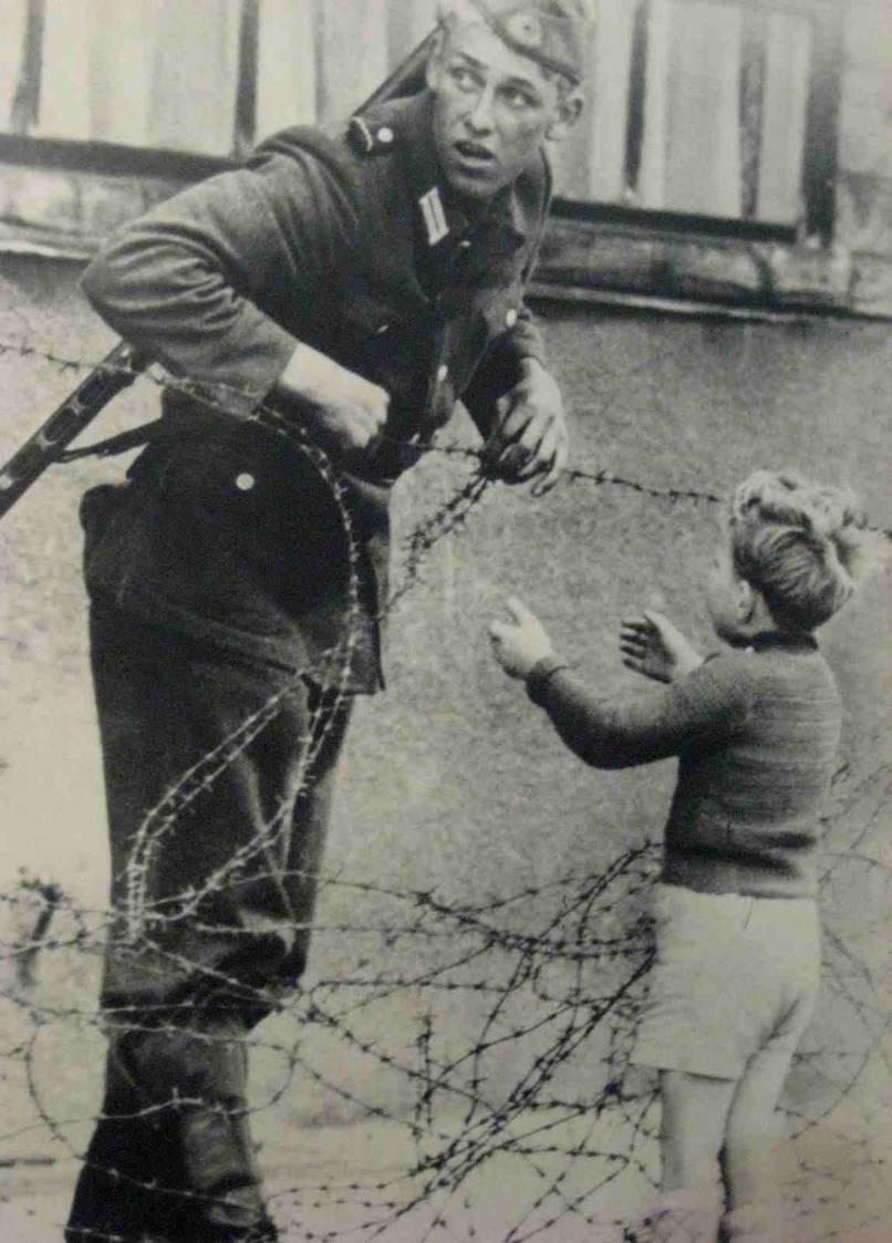 An East German soldier ignores orders to let no one on the other side of the newly formed "Berlin Wall," but allows this boy to pass who was separated from his family. [Cold War, 1961]