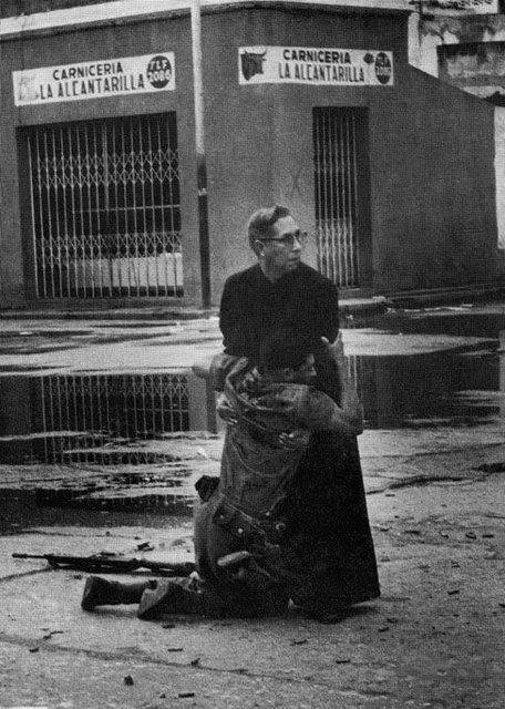 A priest comforts a wounded soldier as a shots are fired all around them. [El Porteñazo Uprising, Venezuela, 1962]