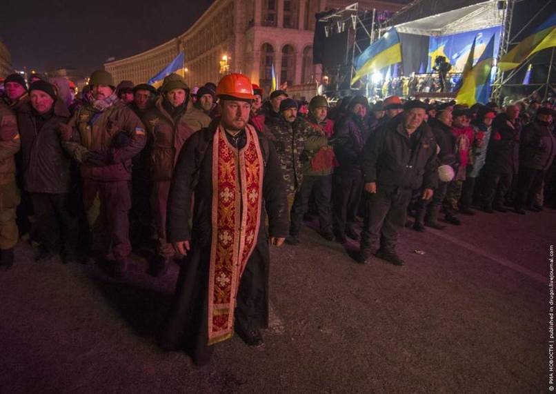 A courageous priest stands as a human shield between law enforcers and protesters. [Ukrainian Revolution, 2013]