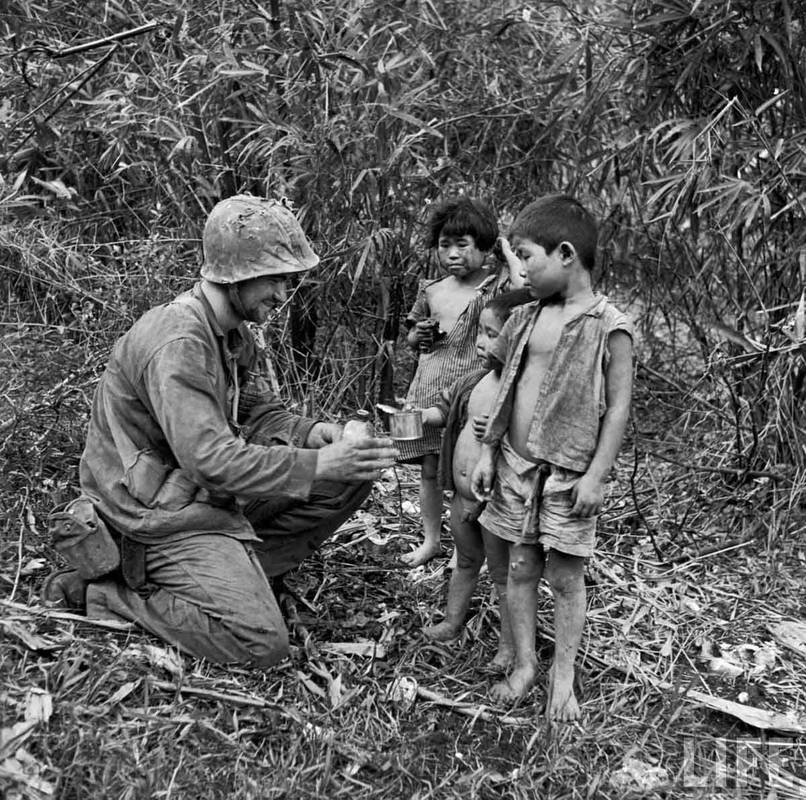 A soldier shares water and food with three children on Saipan. [c. July, 1944]