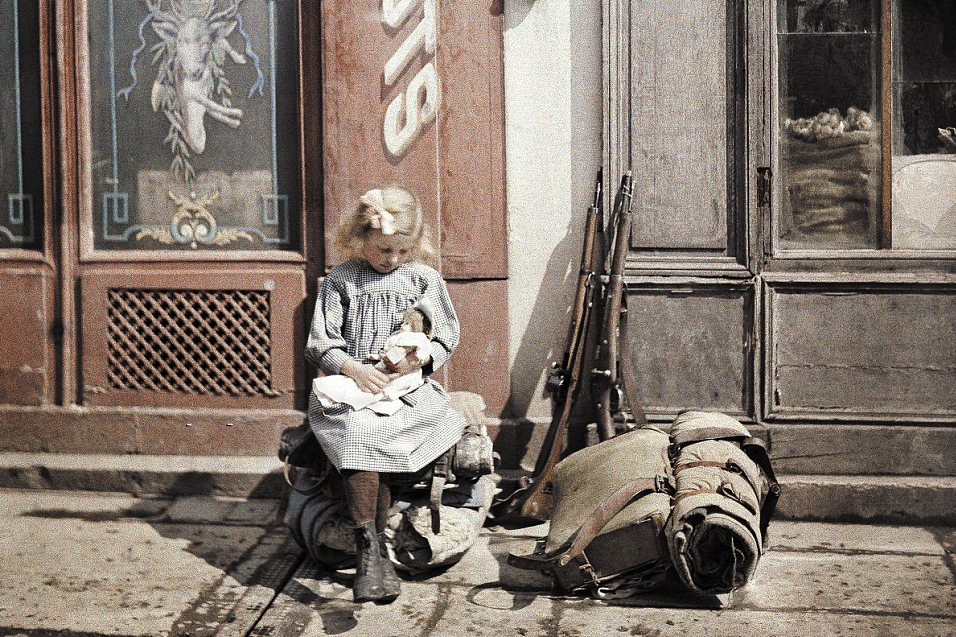 A young girl plays with her doll whilst sitting next to two guns and a military knapsack on a street in Reims, northern France: