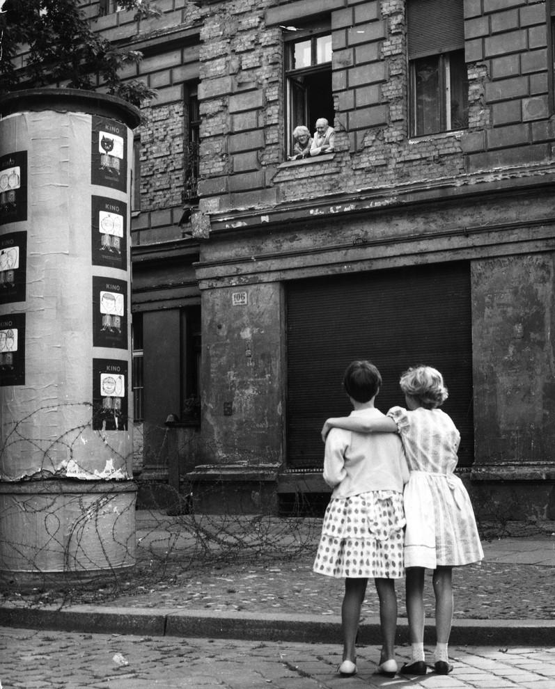 In August 1961, two young girls speak with their grandparents in East Germany over a barbed wire fence, a barricade which later became the Berlin Wall