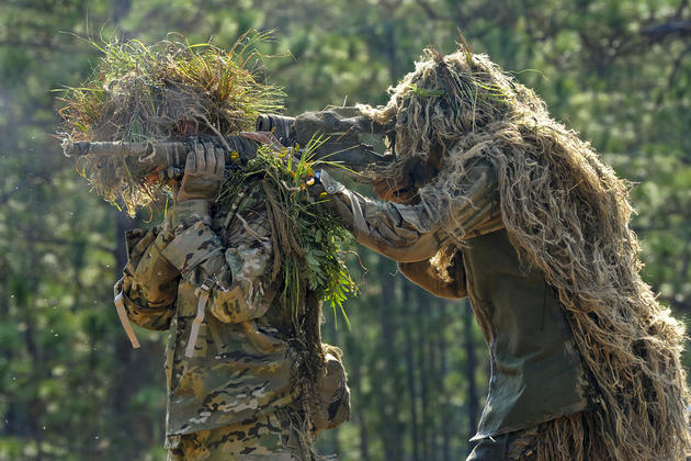Two snipers wearing ghillie suits combine to form an over-the-shoulder firing position during competitive shooting at the 10th Annual International Sniper Competition on Fort Benning, Ga., Oct. 14, 2010. A ghillie suit is a type of camouflage from cloth or fibers, with the name originating from gille, the Gaelic word for servant.
