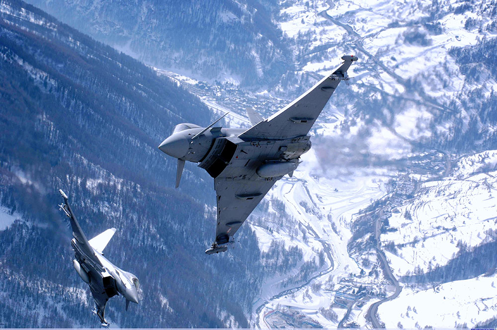 Two Eurofighter Typhoon jets maneuver amid the snowy peaks of the Alps.
