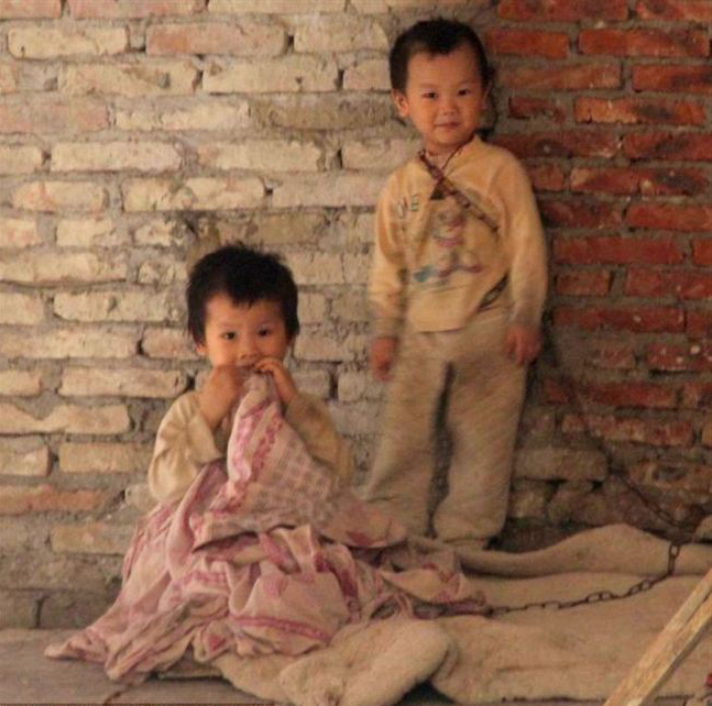Chinese children living in chains because working parents cannot afford childcare and medical fees. Two young children are left chained up on a building site in Guangzhou in southern China while their parents work. The small boy and his sister, aged three and four, are restrained by heavy chains so they cannot run off or be taken away by strangers.