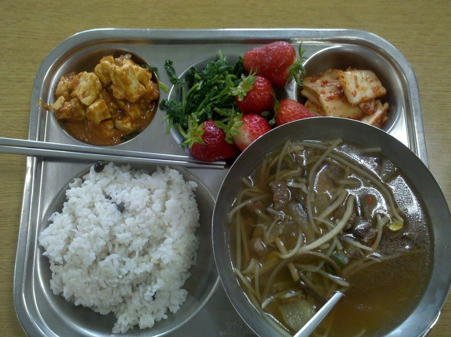 Korean Middle School Lunch- Left to right top down- fresh tofu in sauce, parboiled spinach and garlic in sesame oil, farm fresh strawberries, on-site fermented kimchi, mixed black beans and rice, beef soybean sprout soup with assorted vegetables.