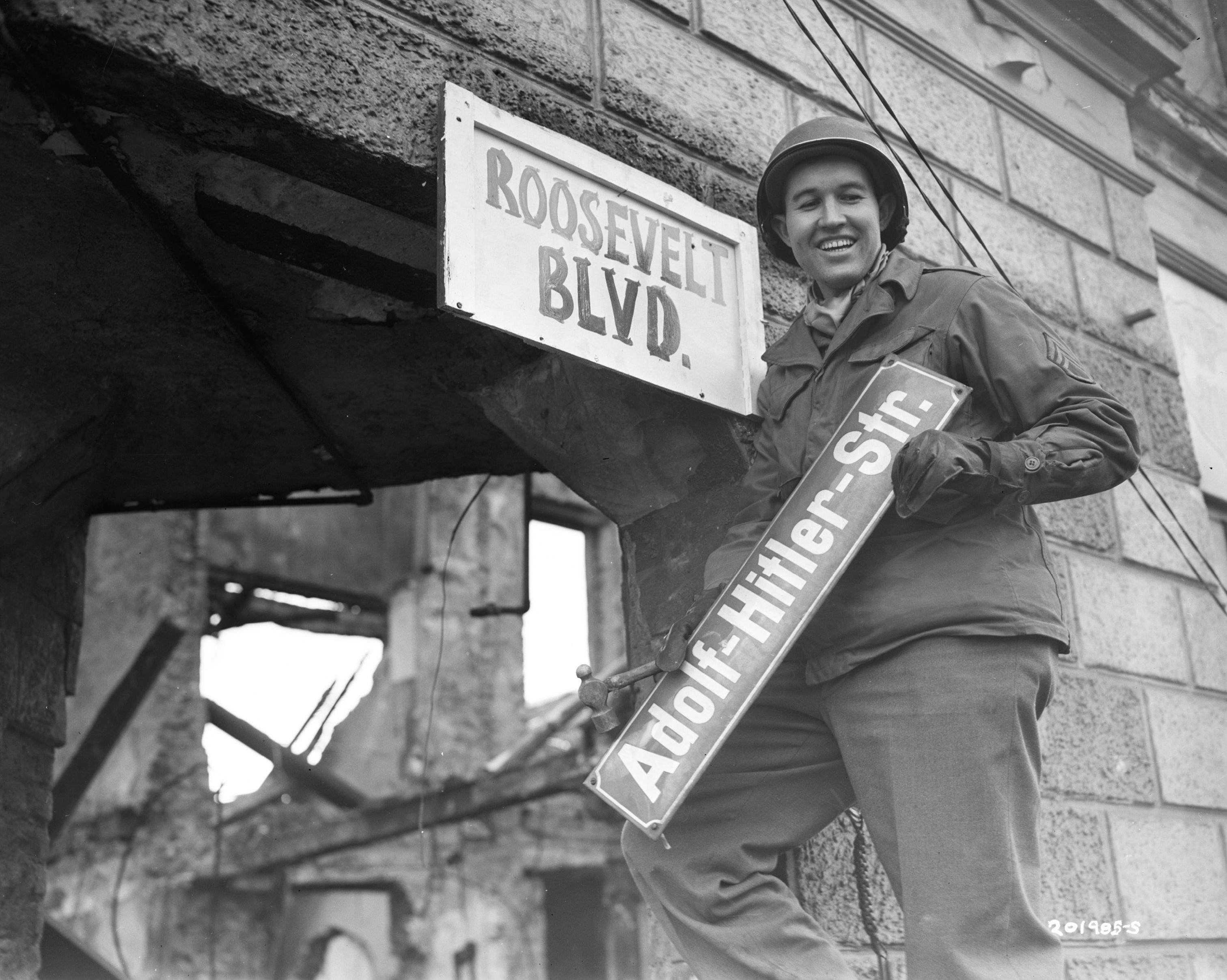 American soldier taking down a sign from a street named after Adolf Hitler in 1945