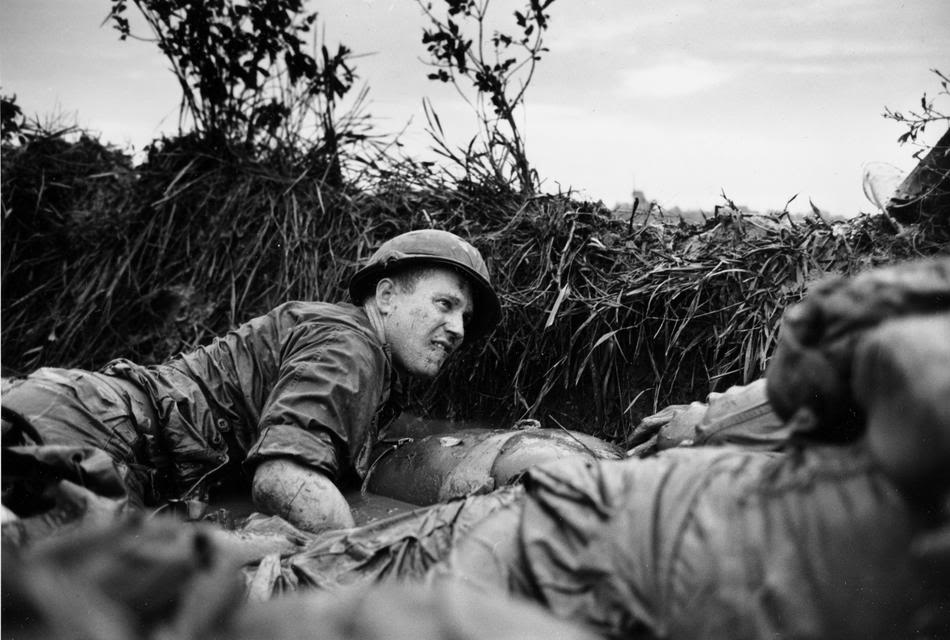 Pinned down by gun fire, a U.S. medic looks over a wounded comrade, Phu Loi, South Vietnam, 1966