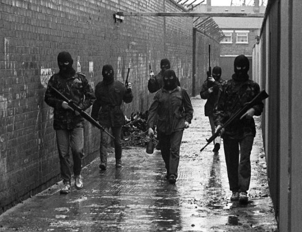 A squad of IRA volunteers moving through a Belfast alleyway. The volunteer in the middle is carrying an anti-tank drogue grenade. Northern Ireland, 1980s.