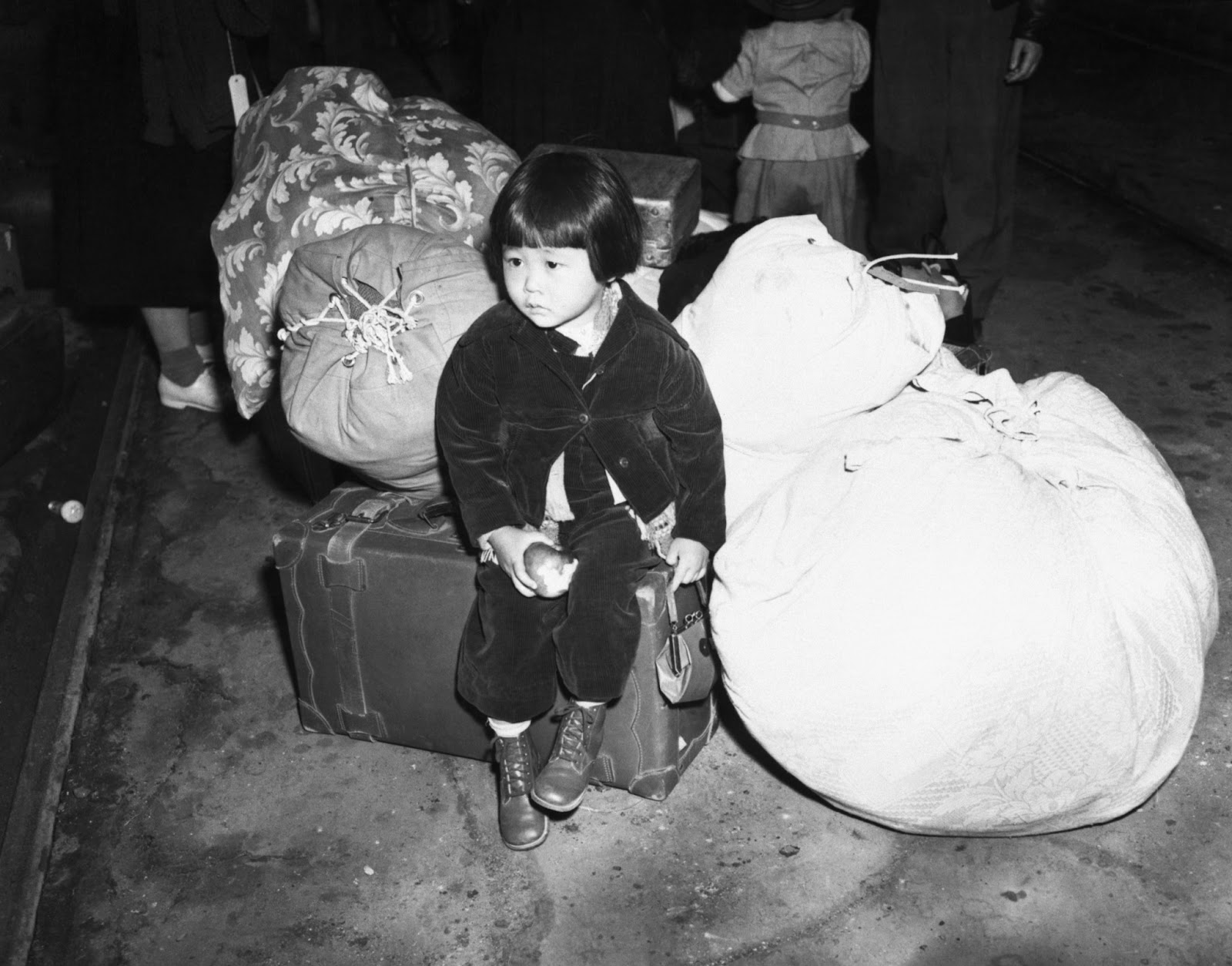 A little American girl of Japanese ancestry waits with the family baggage before being evacuated to the internment camps in the spring of 1942, California