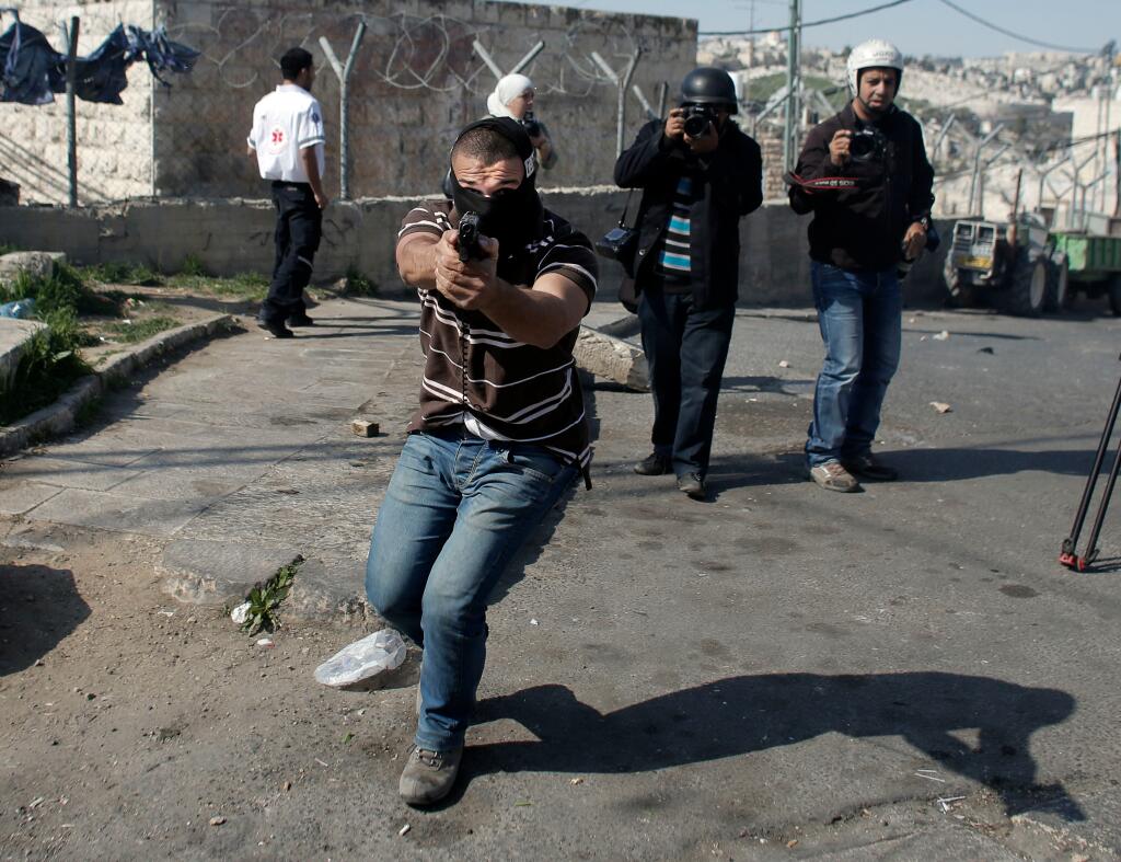 A masked Israeli policeman points a gun at AFP photographer Ahmed Gharabli, who doesn't stop taking pictures.