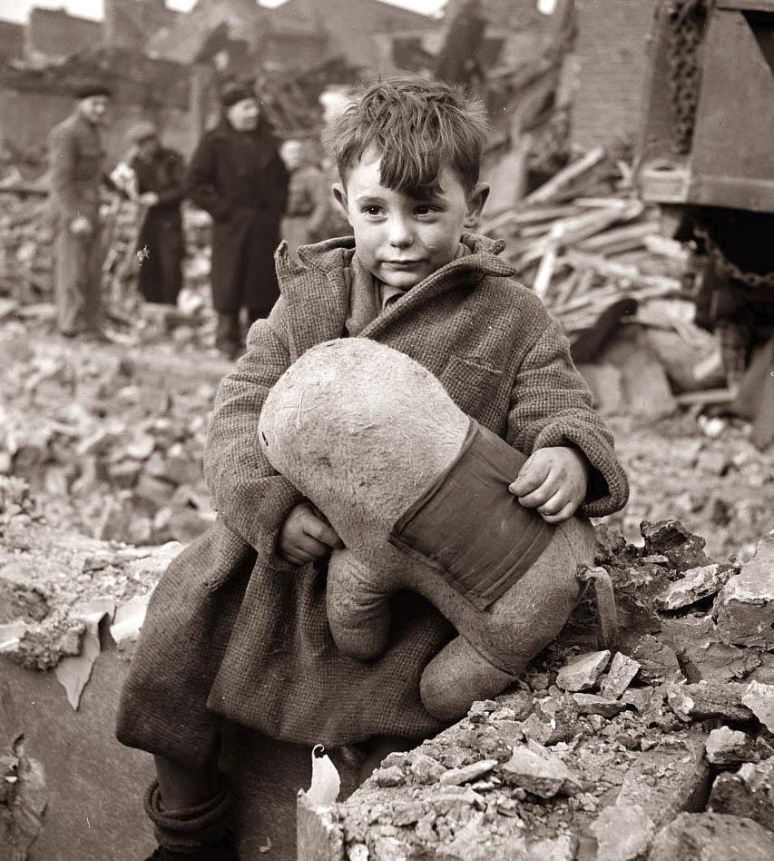 Abandoned boy holding a stuffed toy animal amid ruins following German aerial bombing of London, 1940