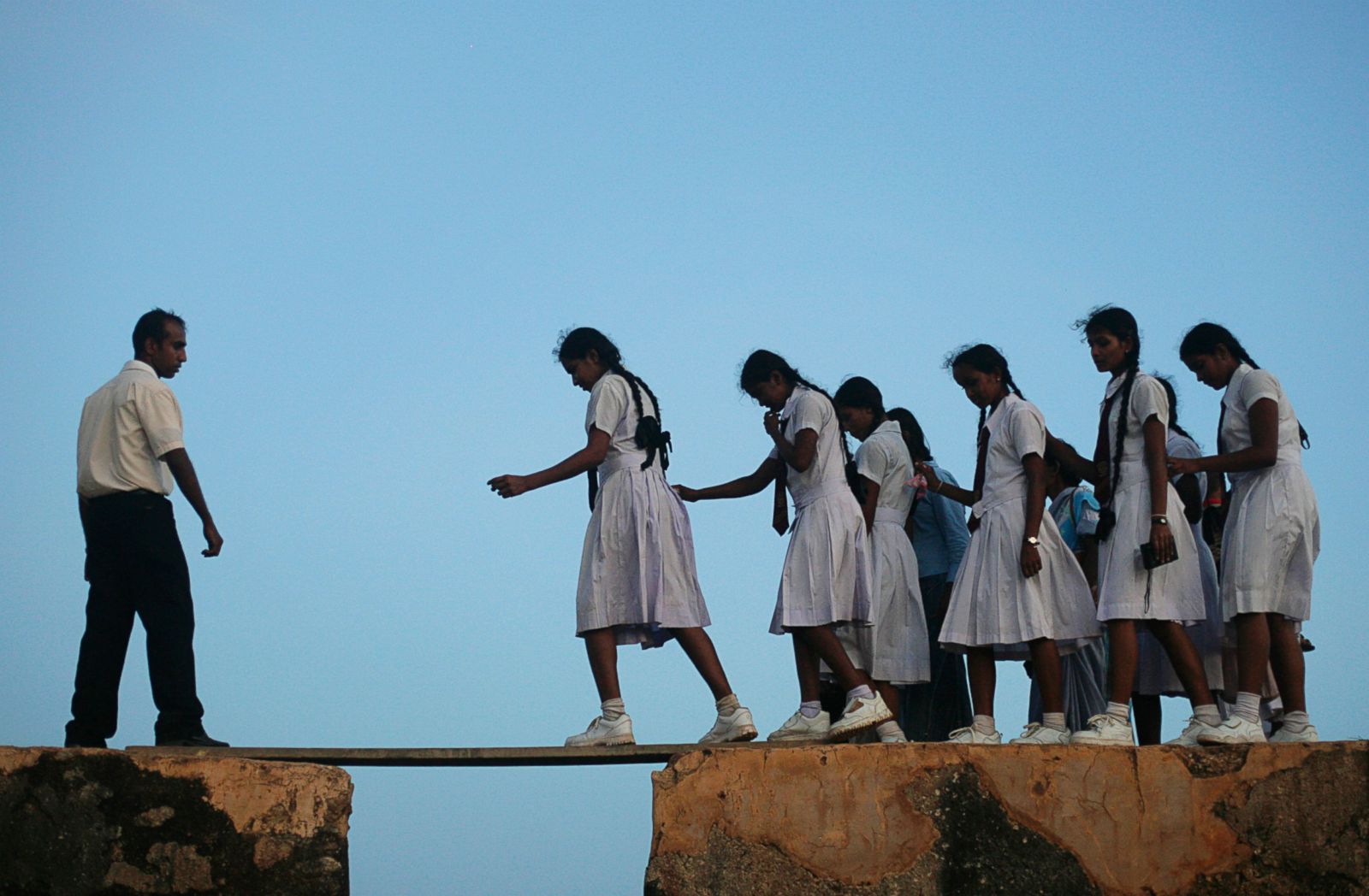 School girls walking across a plank on the wall of the 16th century Galle Fort in Sri Lanka
