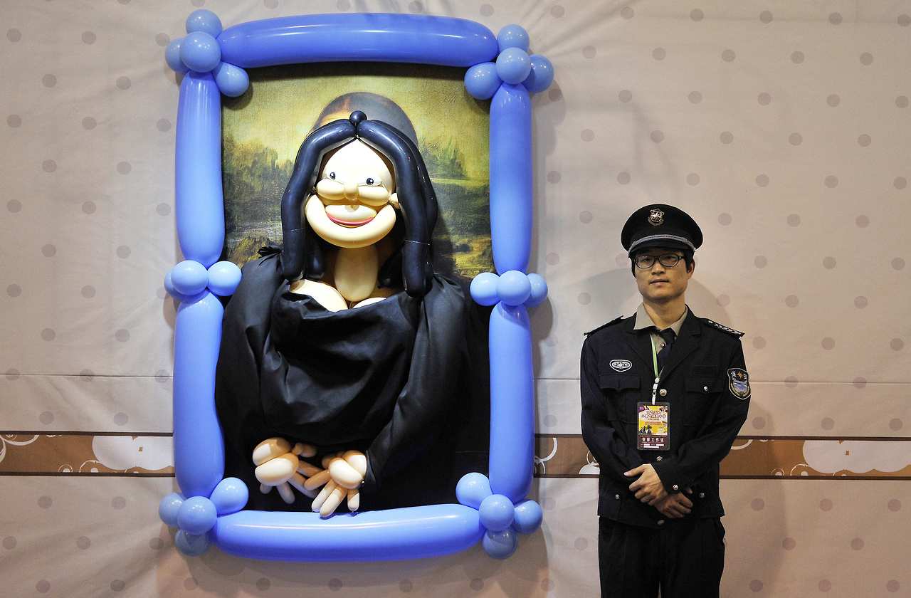 A security guard stands next to a balloon art piece depicting Mona Lisa by Leonardo da Vinci at a balloon-themed carnival in Hefei, China.