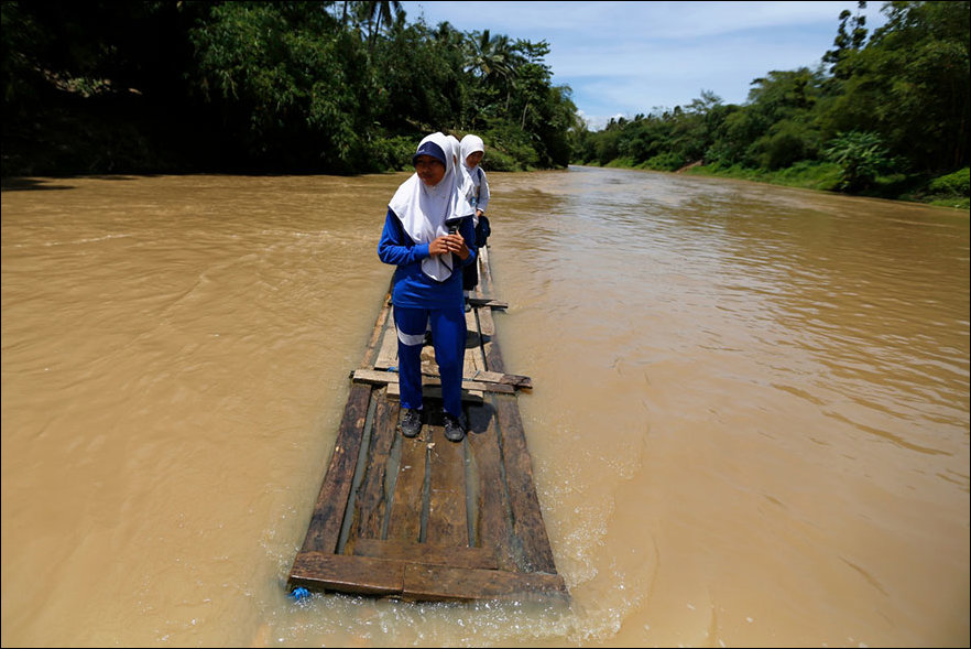 Pupils cross the river on a makeshift bamboo raft in Indonesia.