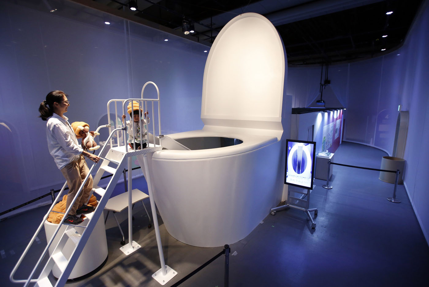 A girl wearing a feces-shaped hat prepares to slide down into a 16-foot toilet at an exhibition entitled, “Toilet!”.