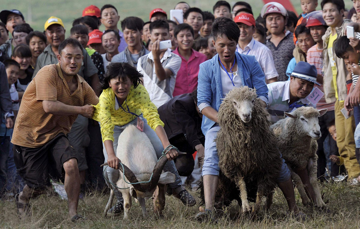 People look on as participants ride goats and sheep during a race to celebrate a local festival in Fengshan, China.