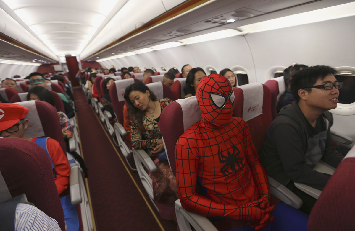 A  air crew member dressed as Spiderman during an onboard Halloween celebration sits next to more regularly dressed passengers.