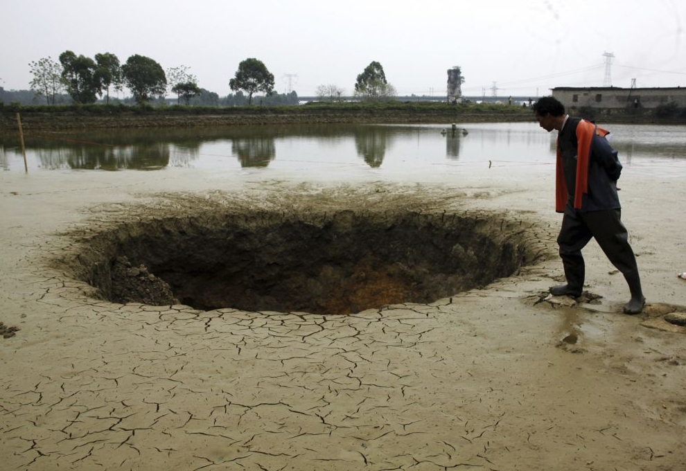 A man looks into a sinkhole which appeared in his fish pond in Guiping