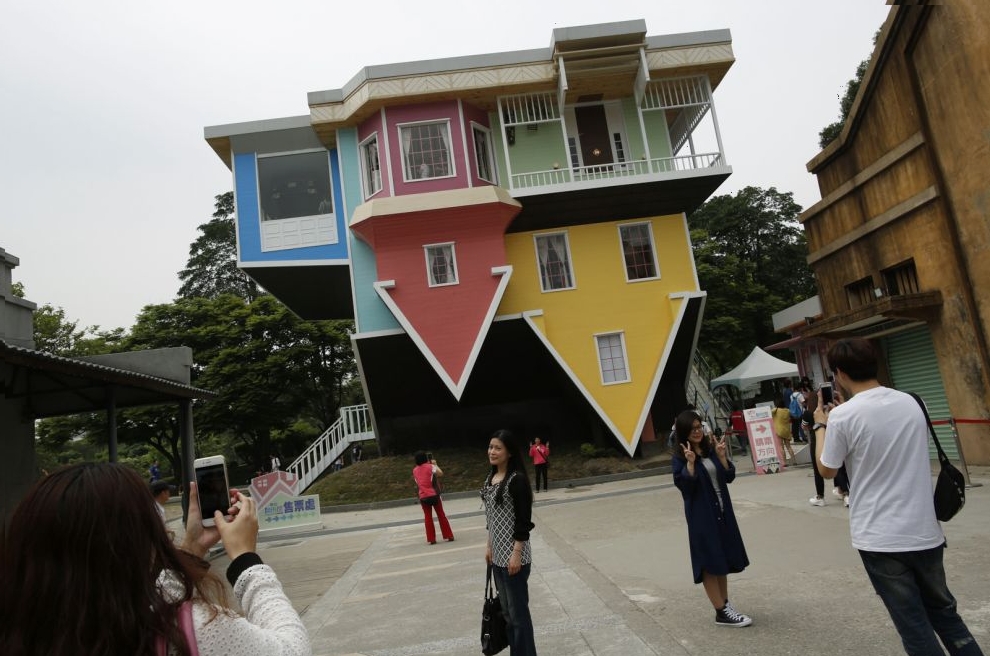 Visitors pose in front of a three story upside-down family sized house at the Huashan Creative Park in Taipei