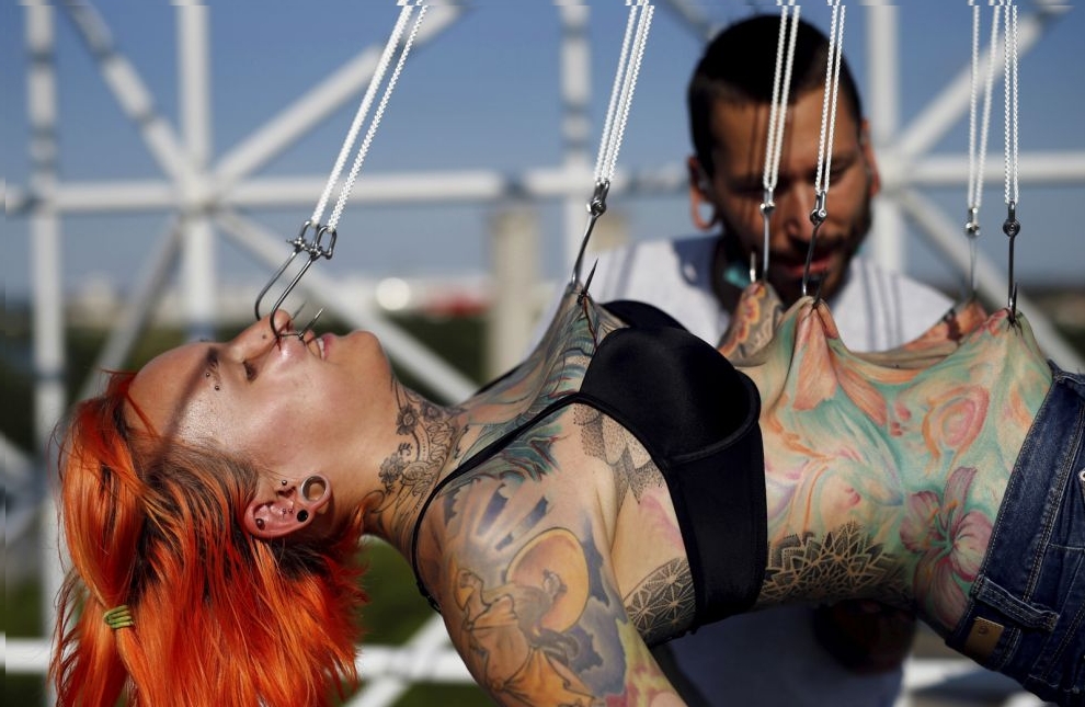 Professional body artist Dino Helvida (R), 27, inspects Kaitlin, 28, from the United States, as she is suspended from hooks pierced through her skin in Zagreb, Croatia June 7, 2016