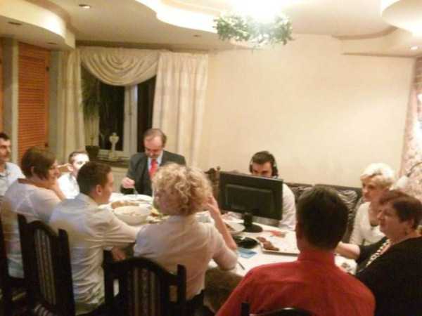 Man at dinner table with his whole family and a full monitor and desktop computer setup