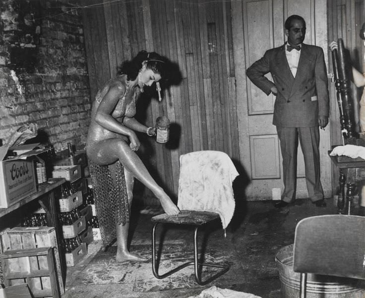 A stripper applies glitter to her body after covering herself in a golden cream before a show in LA, US in 1950.