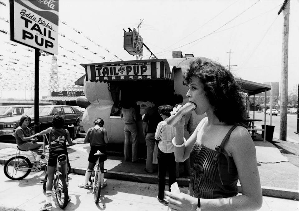 Sigourney Weaver sampling a hot dog outside of Tail of the Pup, a famous hot dog shaped hot dog joint in LA, 1983.