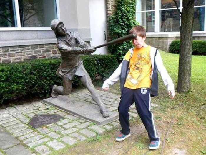 Kid posing next to statue as if it is beating him up.