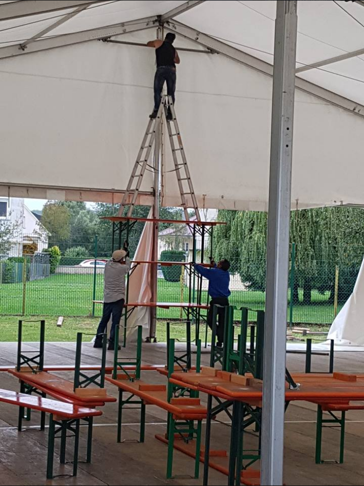 Man on a ladder on top of 3 tables to secure a big tent