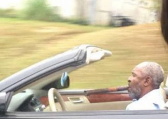 black man driving a convertible with a massive cigar in his mouth