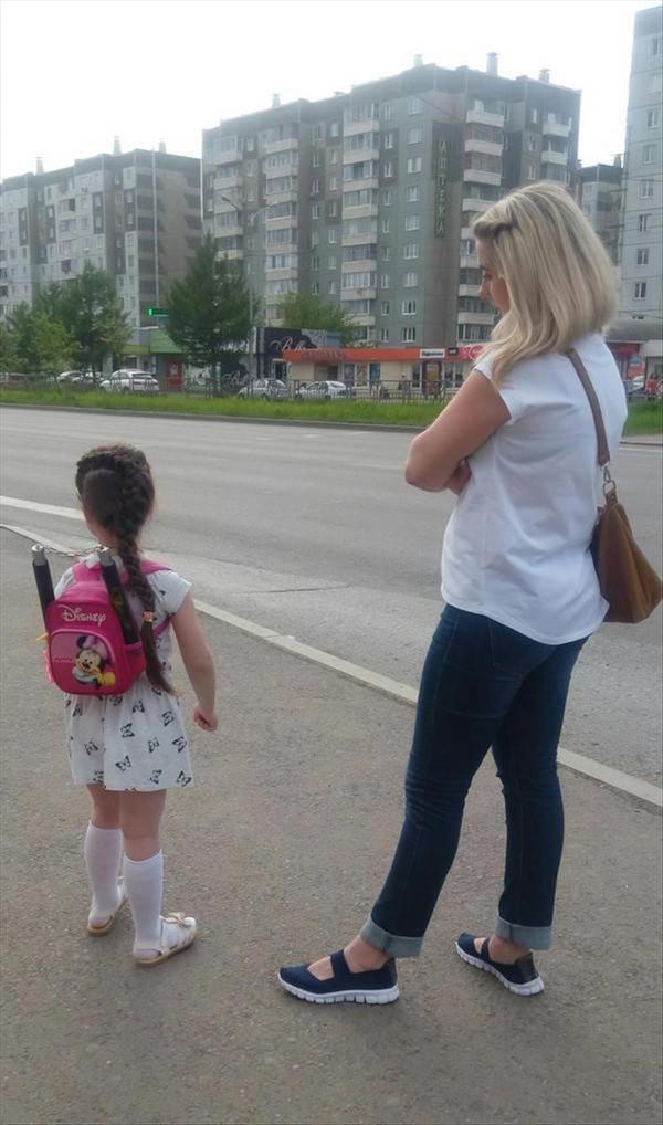funny picture of mom and girl waiting for the bus to school and the little girl has nunchucks in her disney school bag