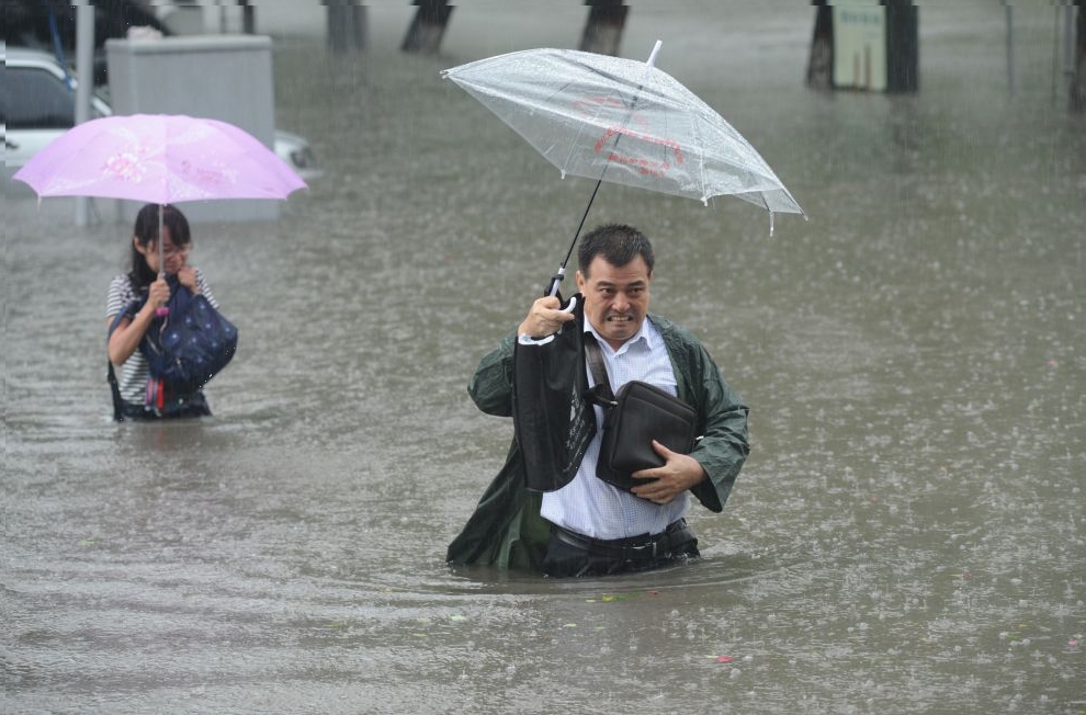 People hold umbrellas as they walk past a flooded street in Taiyuan