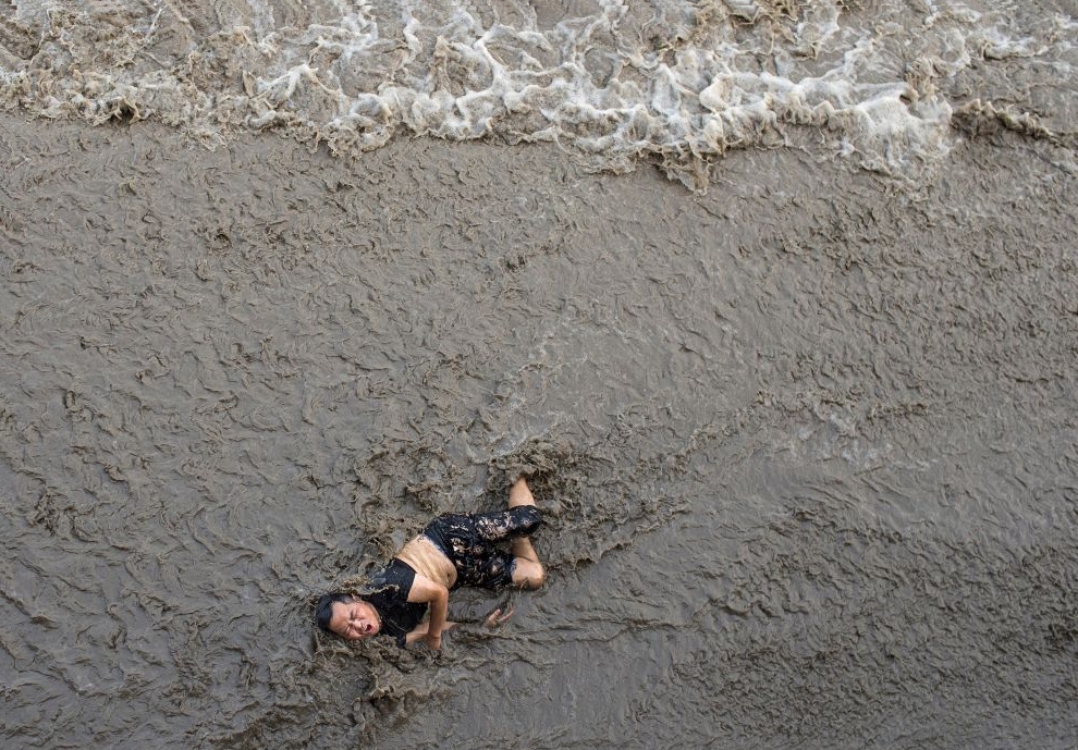 A man who fell off a bridge while waiting to watch tidal wave struggles as waves come towards him, on the banks of Qiantang River in Hangzhou