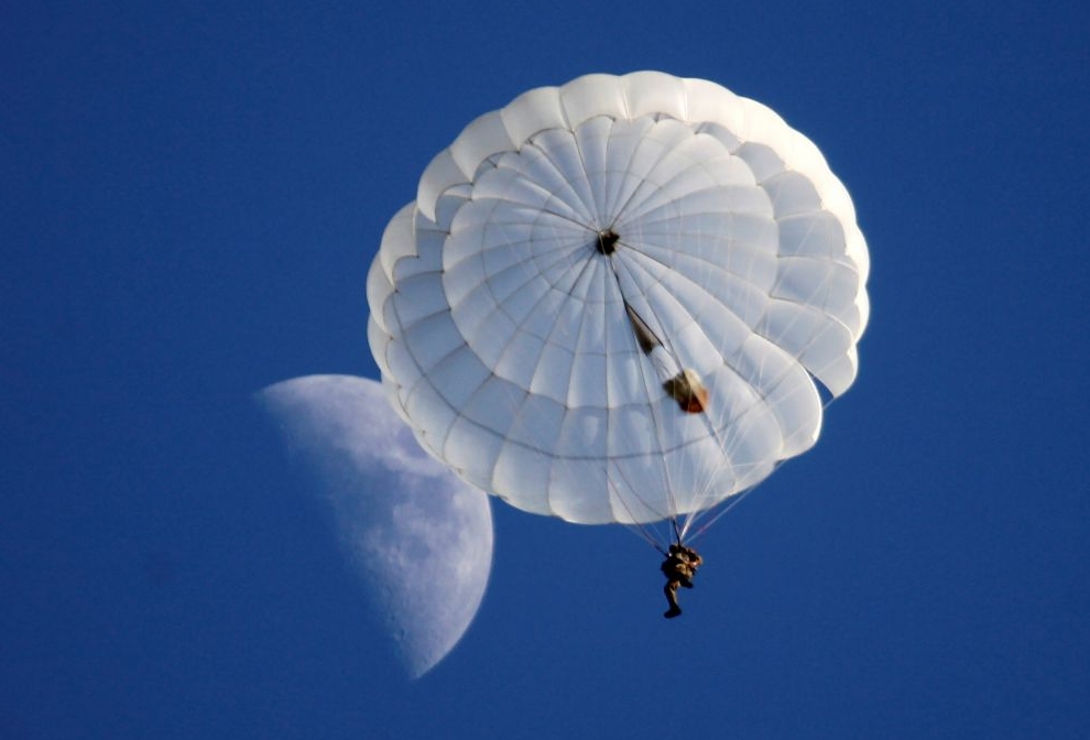A student of the General Yermolov Cadet School is pictured after jumping with parachute from an airplane, as the moon is seen in the sky, in the village of Novomaryevskaya outside the southern city of Stavropol