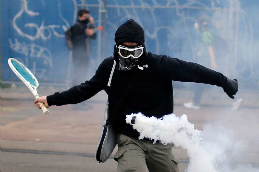 A protester uses a tennis racket to return a tear gas canister during a demonstration to protest the government's proposed labor law reforms in Nantes