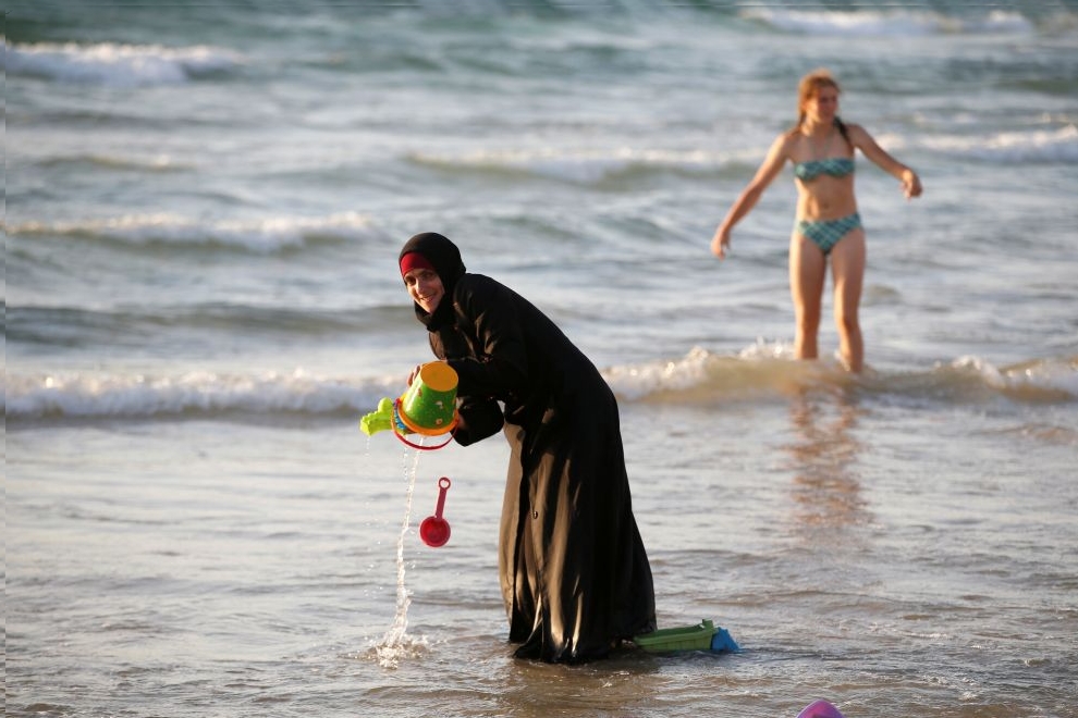 Muslim woman wearing a Hijab stands in the waters in the Mediterranean Sea as an Israeli stands nearby on the beach in Tel Aviv