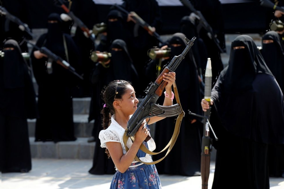 Girl holds a rifle in front of women loyal to the Houthi movement taking part in a parade to show support to the movement in Sanaa, Yemen