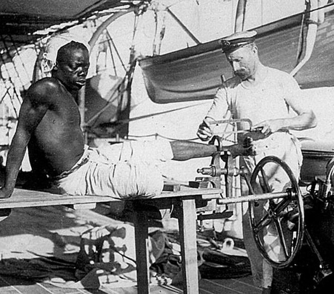 Sailor cutting slaves ankle shackle, 1900