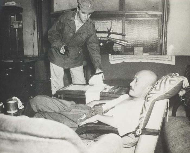 An army intelligence officer attends to Hideki Tojo, the prime minister of Japan during WWII. Tojo attempted to shoot himself in the heart as U.S. troops approached his residence to arrest him. The bullet missed his heart and instead went through his stomach. Tojo made a full recovery before being tried, found guilty of war crimes, and executed.