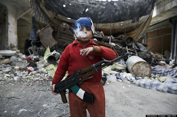Here, an eight-year-old Syrian rebel is pictured with a cigarette and an AK-47 draped over his shoulder.