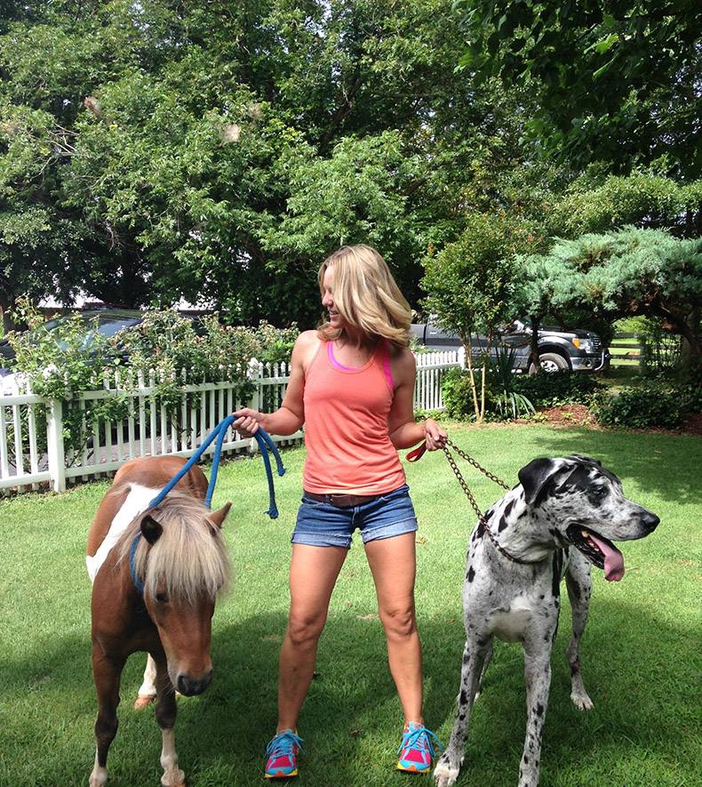 Cute girl holding massive dog and small pony