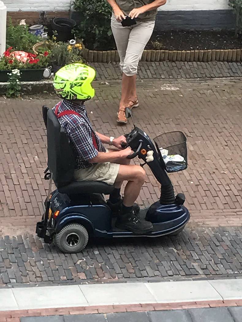 Man on a old man scooter wearing a bright yellow motorcycle helmet